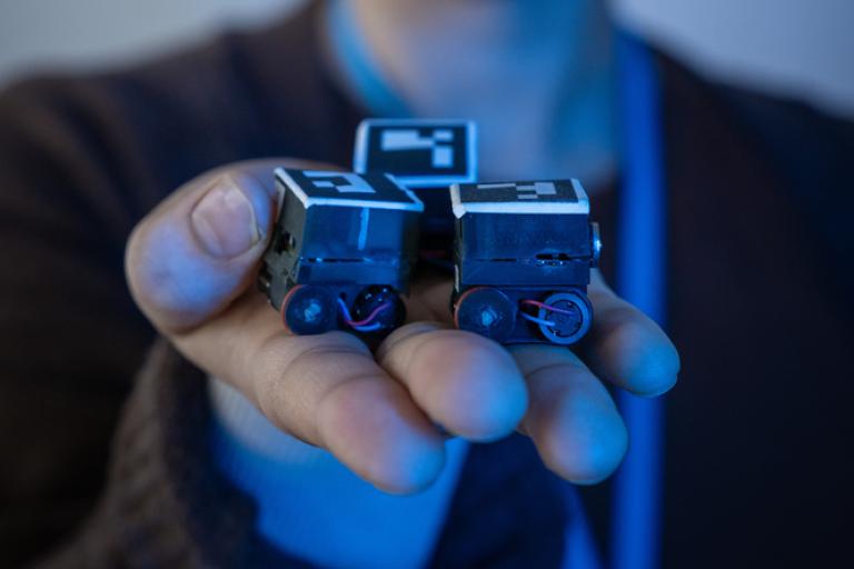 A moody image of a smartly dressed woman holding out her hand, on which rest three tiny robots.