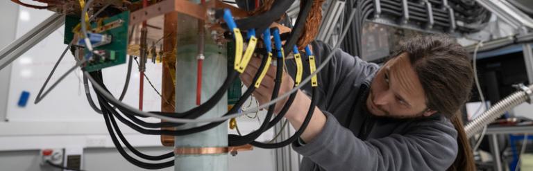 A long haired man ducks under a prototype machine to make adjustments.