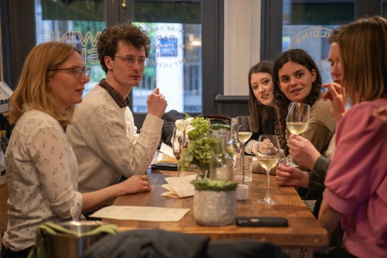 A group of colleagues have an animated discussion at a wine bar.