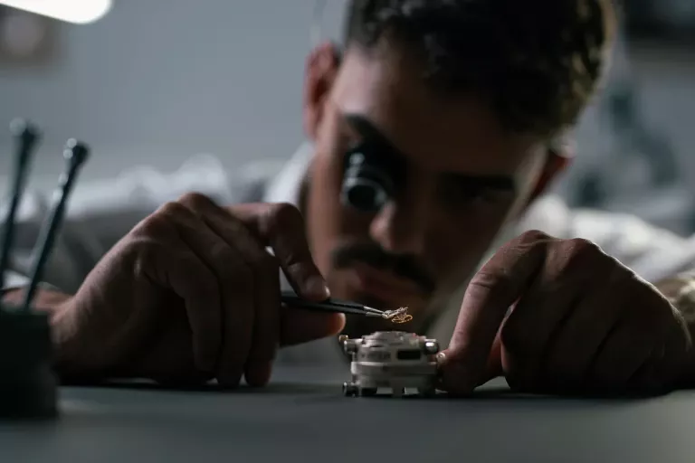 A craftsman uses precision tools to add part of a mechanism to a watch
